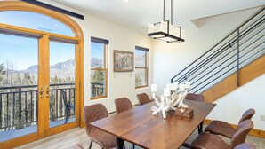 Un comedor amplio con una gran mesa de madera, varias sillas y vistas a montañas a través de un ventanal.
