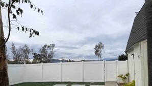 A fenced backyard with a white fence, a paved patio, and a small garden area. - Wine Country Hilltop Home w/Views & Pool & Spa - New Listing! (Temecula)