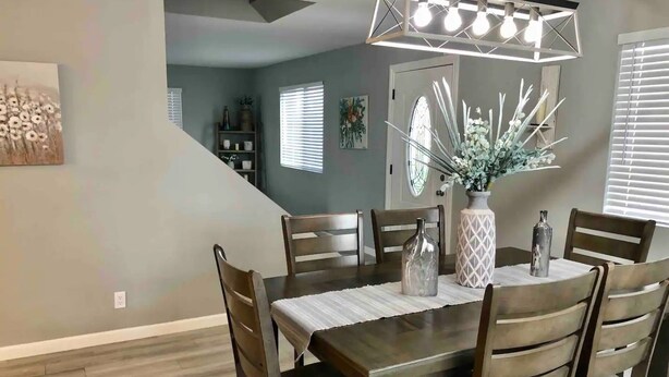 A dining area with a wooden table and chairs, a vase with flowers, and a modern light fixture above. - Wine Country Hilltop Home w/Views & Pool & Spa - New Listing! (Temecula)