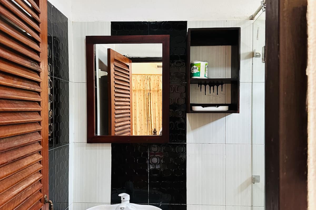 Une salle de bain avec une porte en bois, un lavabo, des toilettes, un miroir et une étagère contenant des articles de toilette.
