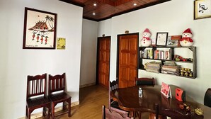 Un comedor con sillas y una mesa de madera, techo de madera con iluminación empotrada, un cuadro en la pared y una estantería con libros y adornos.