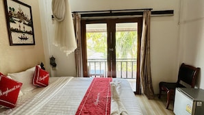 Habitación de hotel con cama, escritorio pequeño, silla, balcón y puerta.