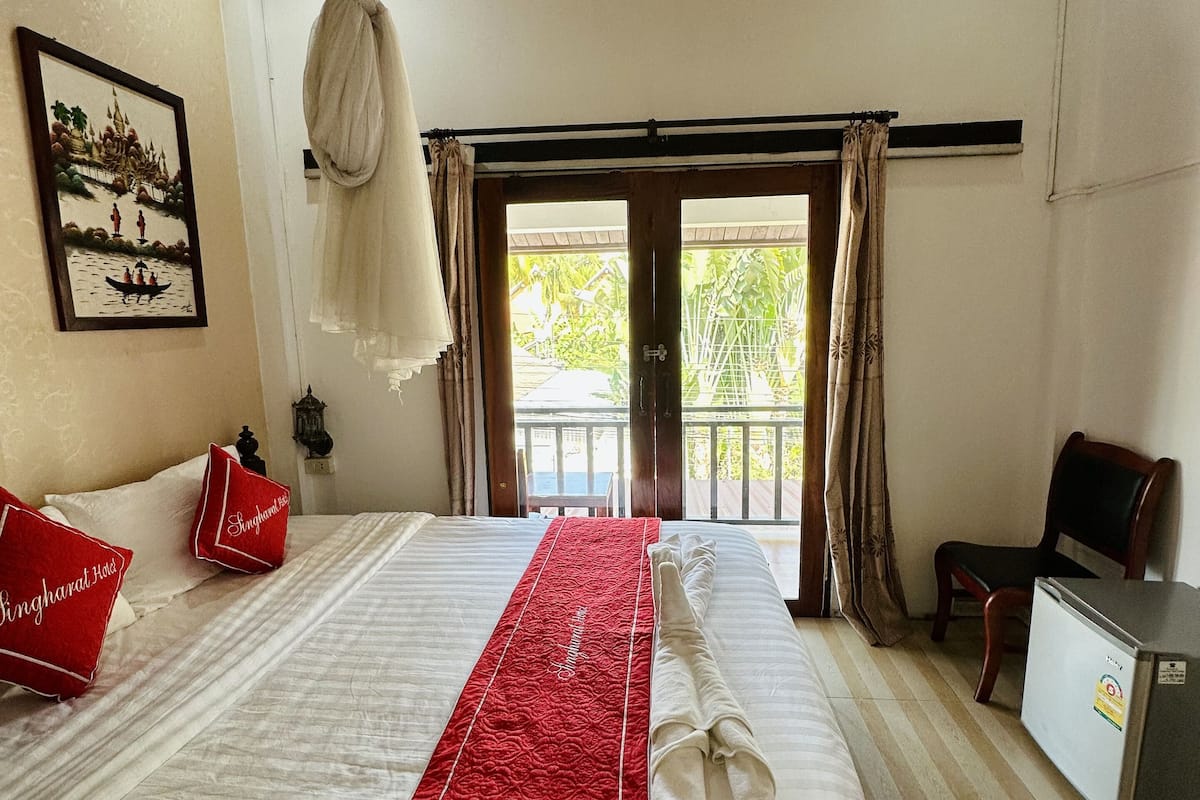 Une chambre d’hôtel avec un lit, un petit bureau, une chaise, un balcon et une porte.