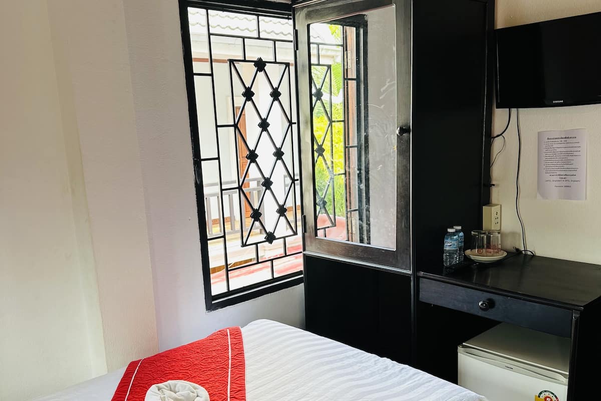 Une chambre d’hôtel équipée d’un lit, d’un bureau, d’un réfrigérateur, d’une fenêtre avec une grille en métal et d’un téléviseur fixé au mur.