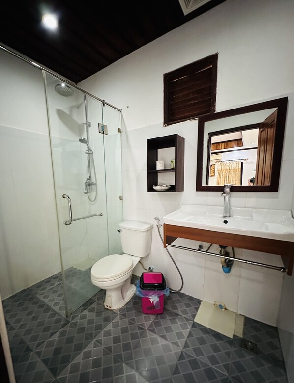 A bathroom with a glass shower enclosure, a white toilet, a sink with a wooden countertop, and a mirror above the sink.