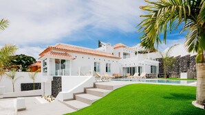 Ett modernt hus med en swimmingpool, en välskött gräsmatta och en mur av sten.