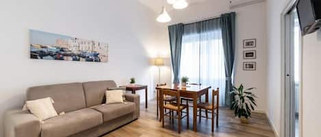 A living room with a sofa, dining table, chairs, a lamp, a TV, and a potted plant.