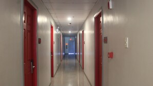 Un long couloir étroit, avec des portes rouges de chaque côté, qui mène à une pièce bleue au bout.