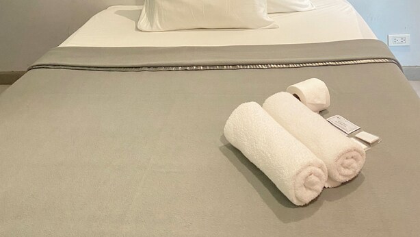 Un lit avec des draps et des oreillers blancs, une couverture grise et deux serviettes enroulées.