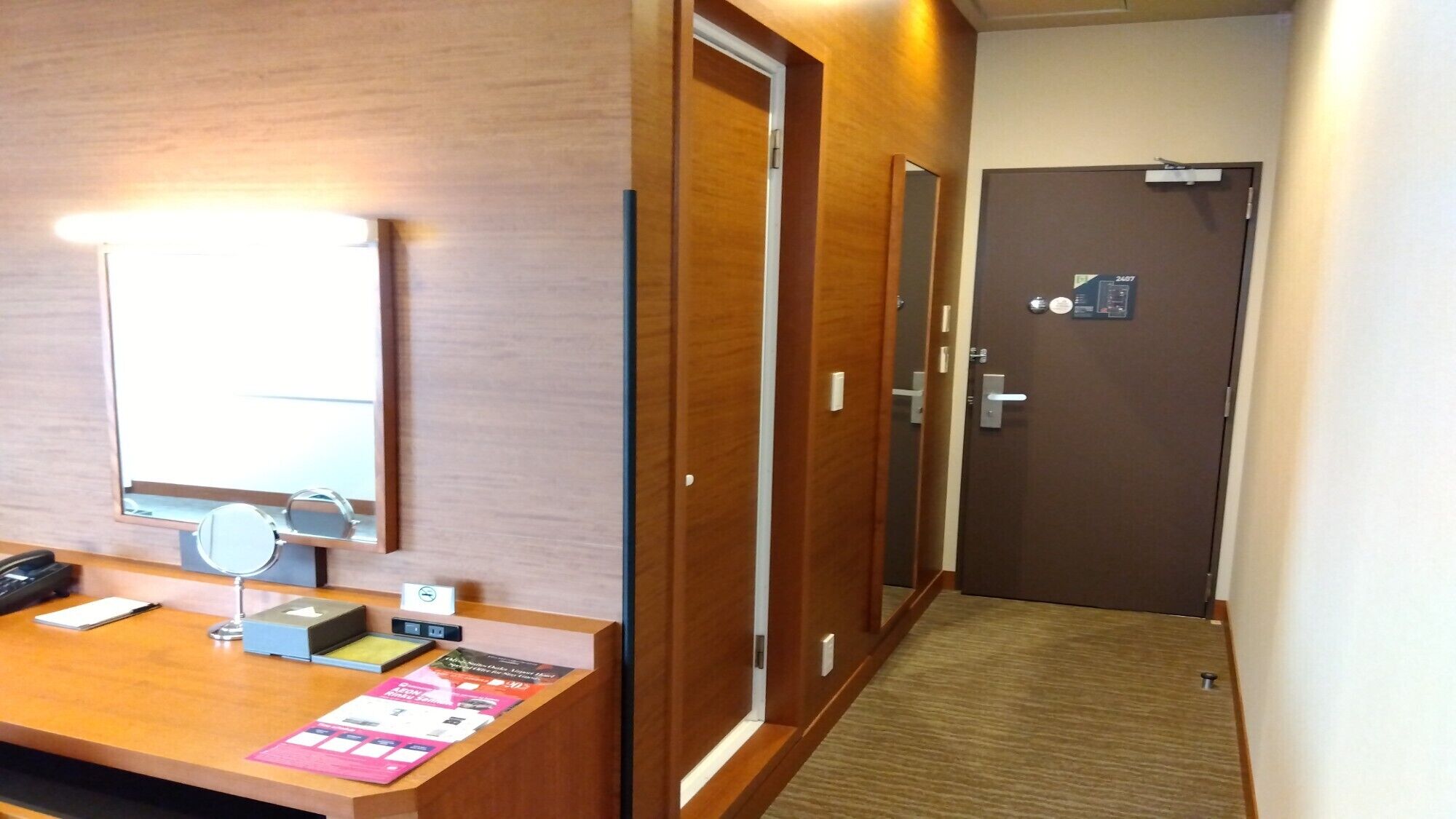 A hotel reception area with a wooden desk, a mirror, a phone, and informational pamphlets.
