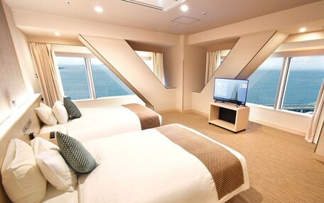 A modern hotel room with two beds, a flat-screen TV, and a view of the sea.