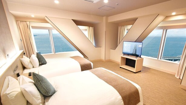 A modern hotel room with two beds, a flat-screen TV, and a view of the sea.