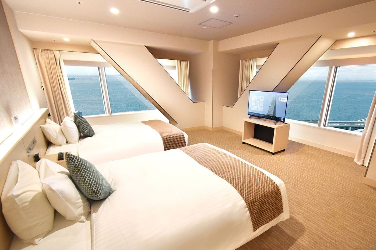 A modern hotel room with two beds, a flat-screen TV, and a view of the sea.