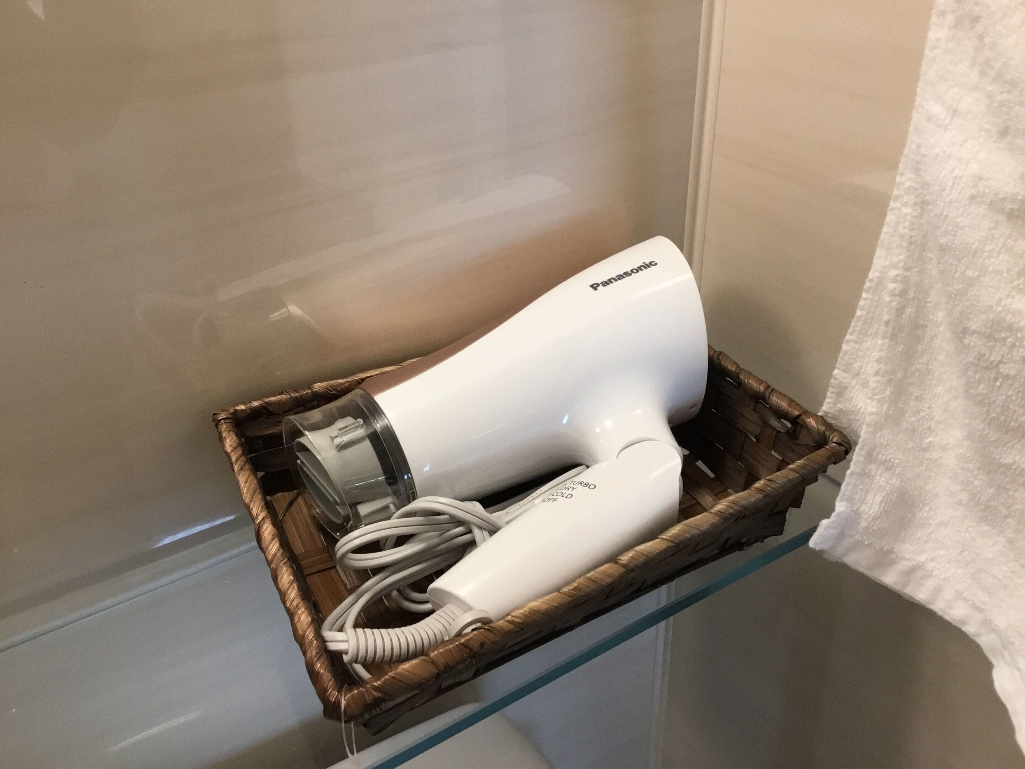 A Panasonic hair dryer in a wicker basket on a glass shelf.