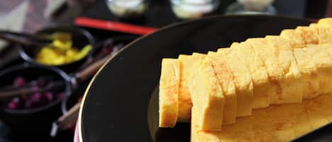 A black plate with neatly cut yellow food, possibly a fruit or vegetable, on a table with a red object and small bowls in the background.