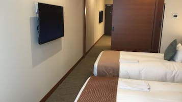 A hotel room with two beds, a television, and a door leading to a hallway.