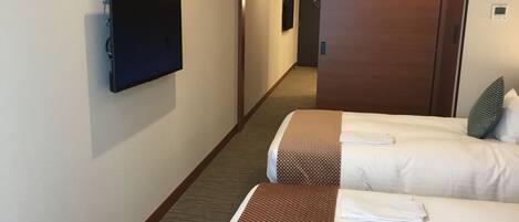 A hotel room with two beds, a television, and a door leading to a hallway.