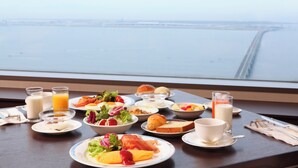 A breakfast table with various dishes and drinks, overlooking a body of water.