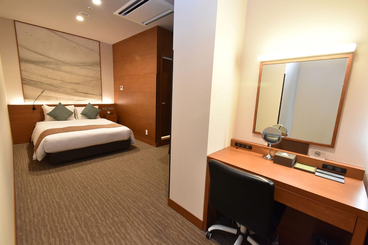 A hotel room with a bed, a desk with a mirror, and a large abstract painting on the wall.