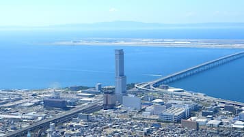 An aerial view of a coastal city with a prominent skyscraper, a long bridge, and a dense urban area with various buildings.
