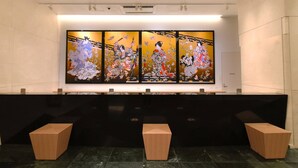 A reception area with a black reception desk, three wooden stools, and a large traditional Japanese painting on the wall. - Odysis Suites Osaka Airport Hotel (Izumisano)