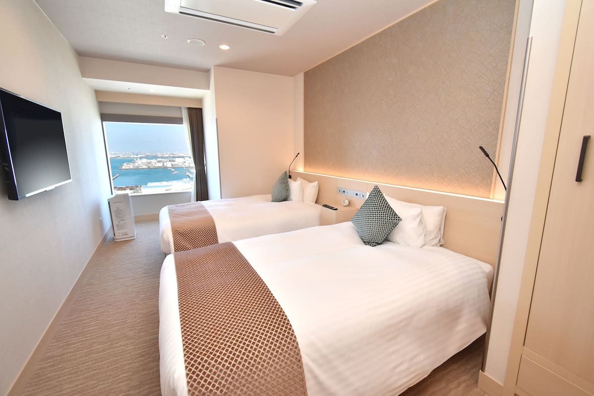 A hotel room with two beds, a TV, and a view of the sea.