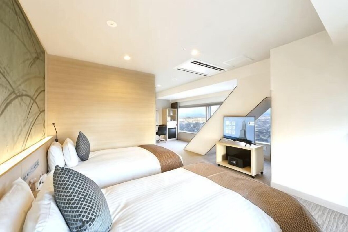 A modern hotel room with two beds, a TV, and a city view.