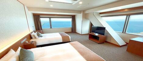 Een hotelkamer met twee bedden, een televisie en grote ramen met uitzicht op zee.