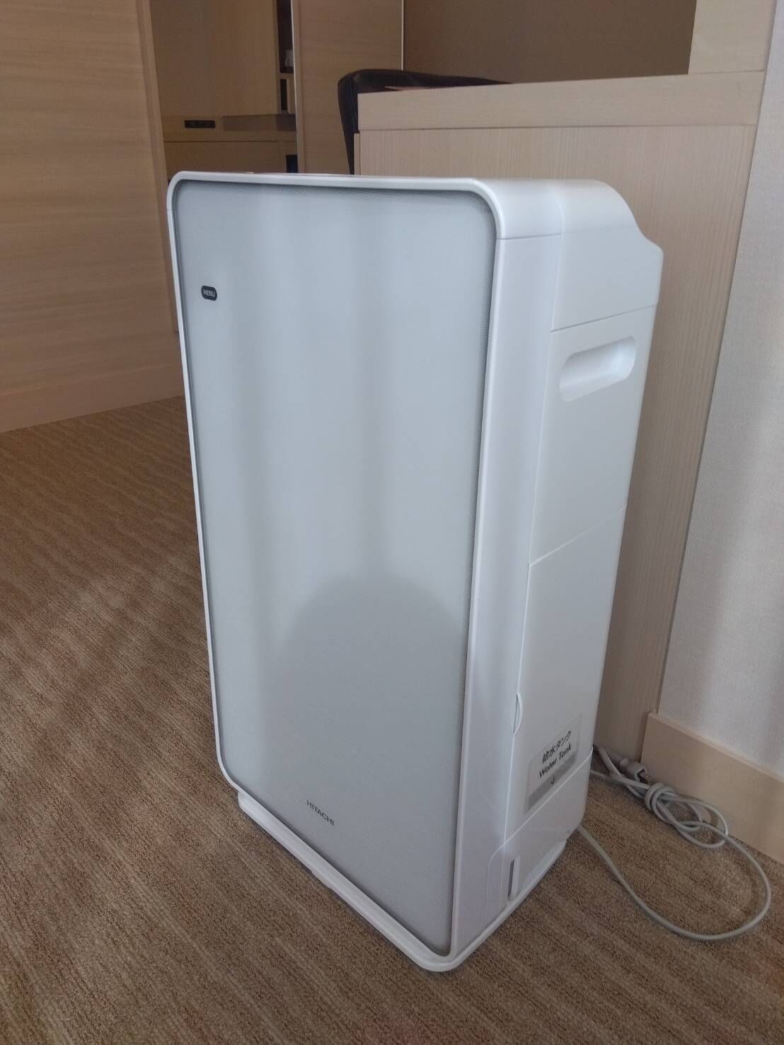 Un refrigerador blanco, compacto y de diseño moderno en una habitación con piso de madera y pared color crema.