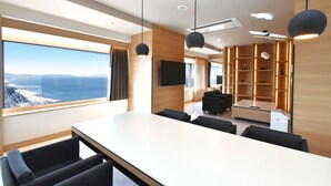 A modern conference room with a large table, black chairs, a TV, and a bookshelf.