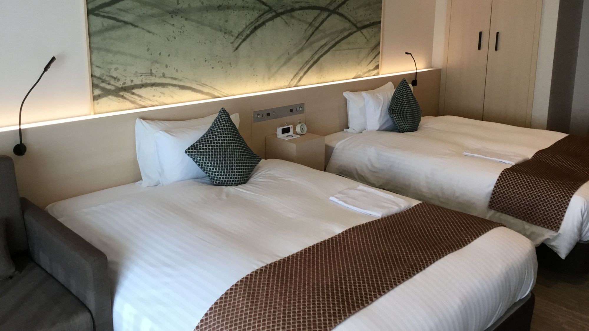 Two beds with white linens, a wall-mounted clock, and a large abstract painting above the beds.