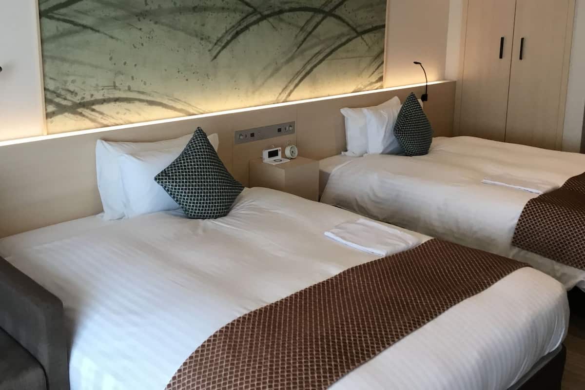 Two beds with white linens, a wall-mounted clock, and a large abstract painting above the beds.