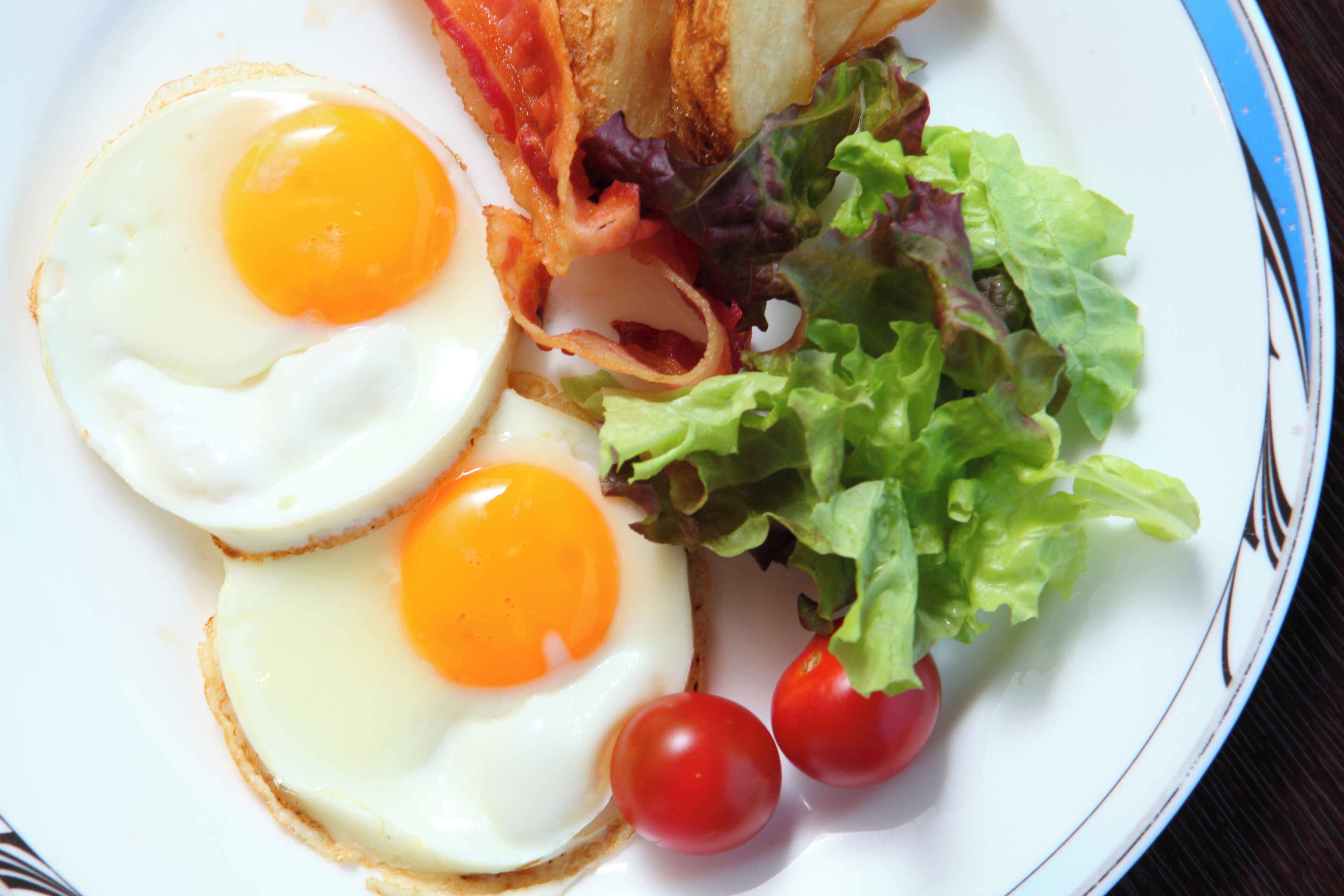A plate with two fried eggs, cherry tomatoes, and a side salad.