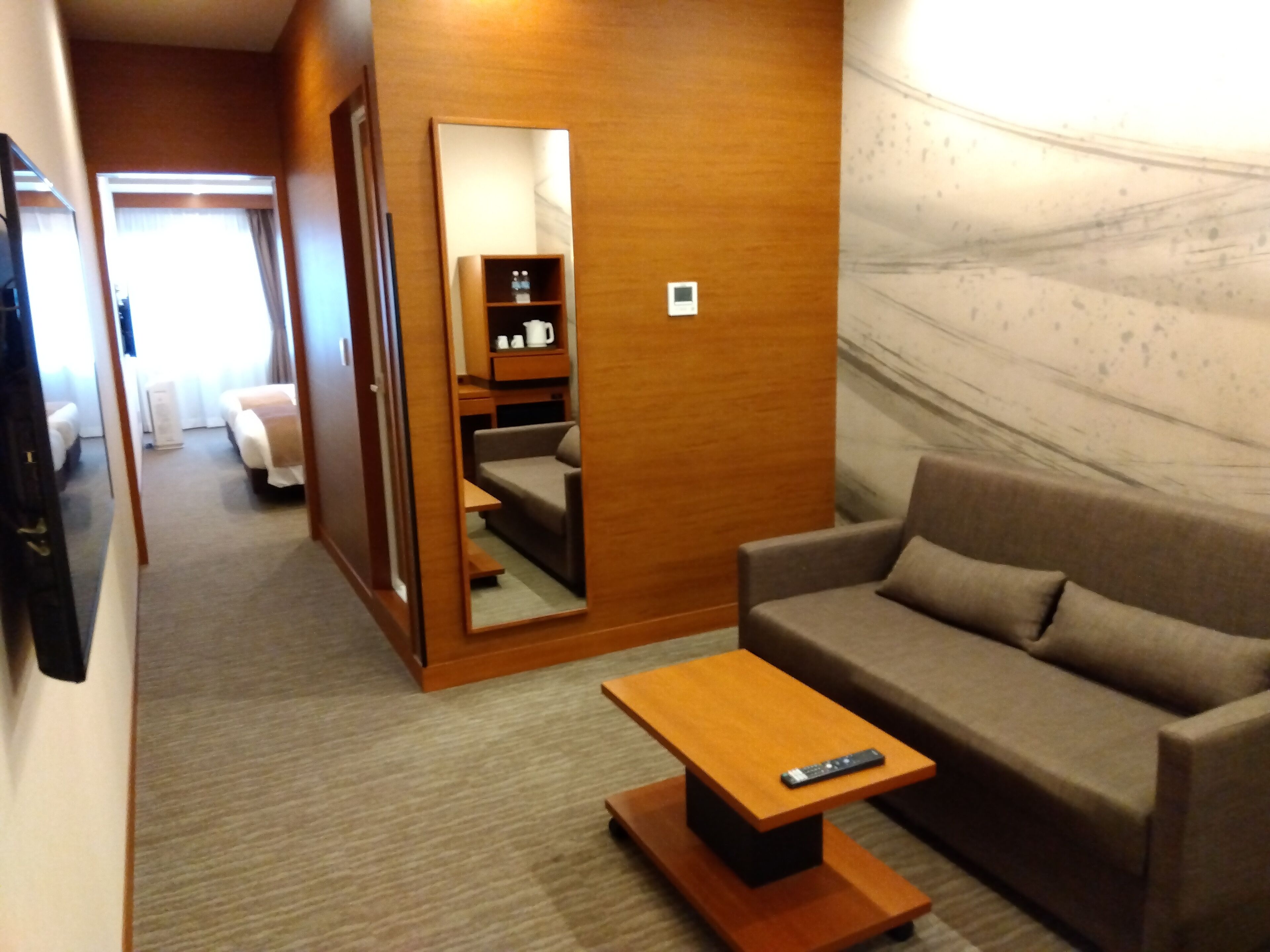 Una habitación de hotel compacta con sofá, una mesita, un espejo y un armario.
