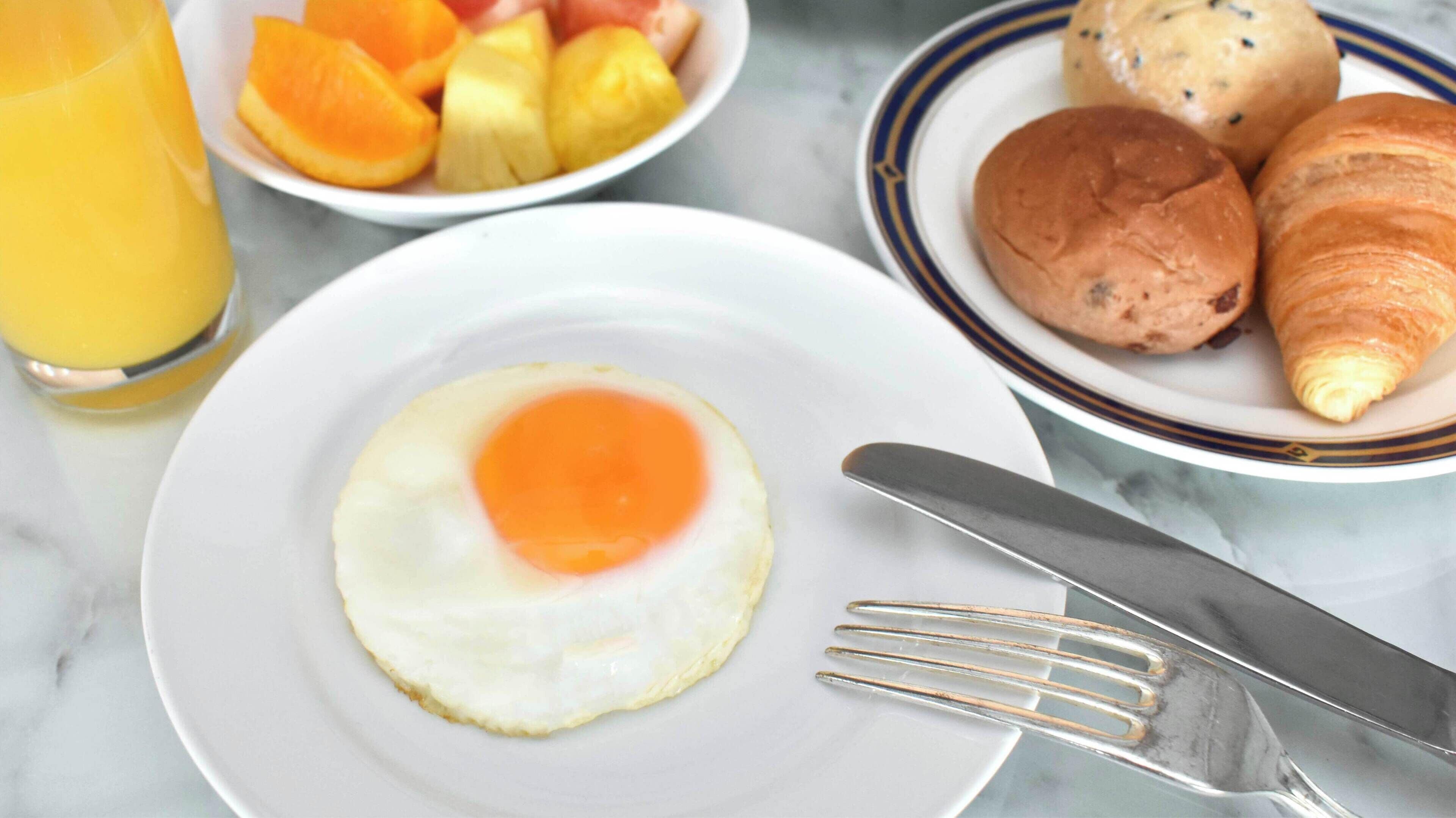 Desayuno con un plato de huevos fritos, un bol de fruta, croissants y un vaso de zumo de naranja.