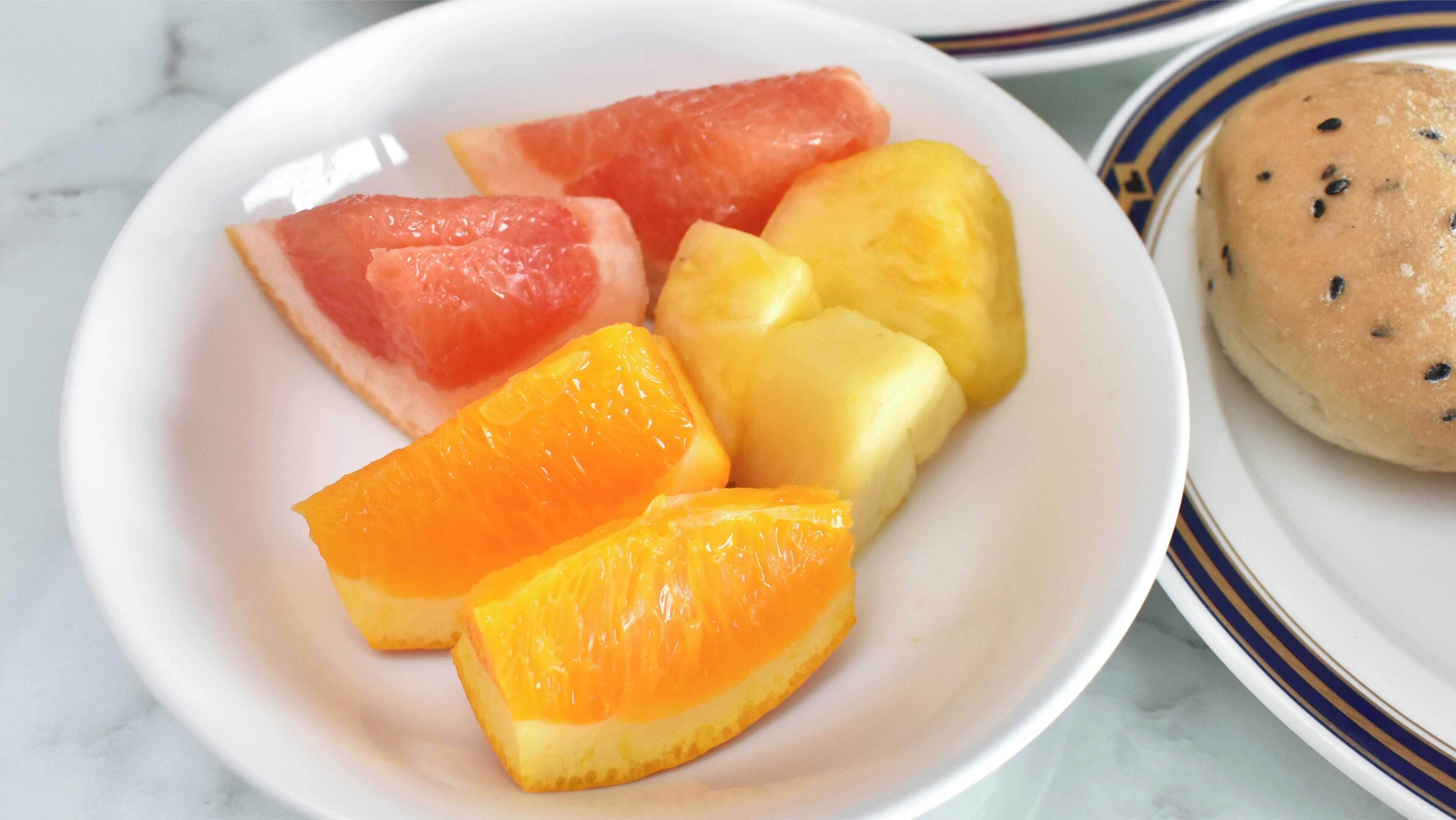A plate with watermelon, pineapple, and orange slices, and a small round bread with seeds.