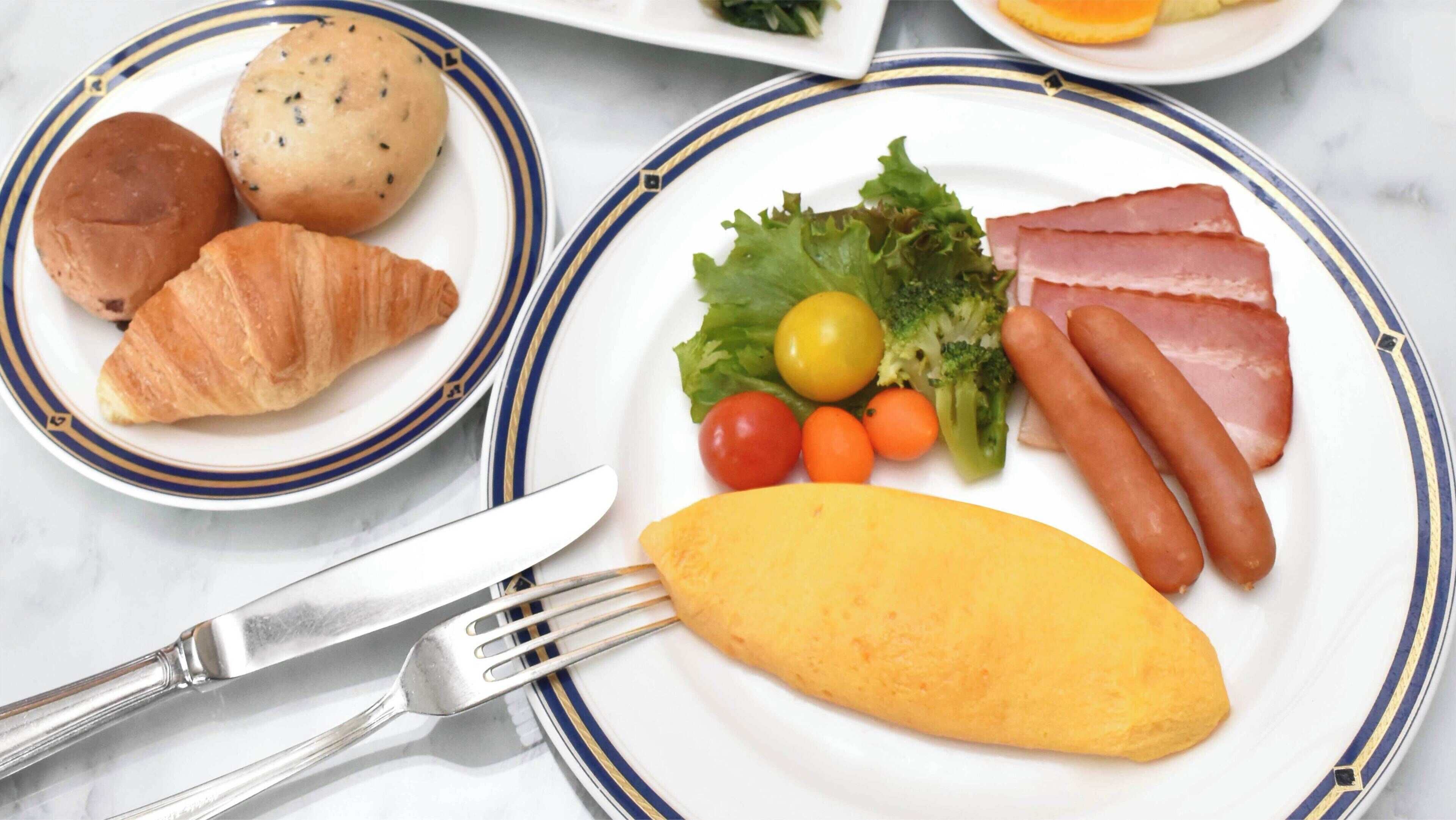 A breakfast plate with croissants, ham, sausages, tomatoes, lettuce, and an omelette.