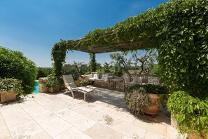 A patio area with a pergola covered in greenery, outdoor seating, and a pool in the background. - 339 I Trulli di Nanì by Perle di Puglia (Ostuni)