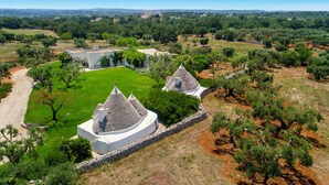 A rural landscape with two white buildings with conical roofs surrounded by olive trees and a clear sky. - 339 I Trulli di Nanì by Perle di Puglia (Ostuni)