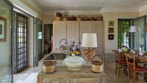 A kitchen with a wooden table, chairs, a stove, and a sink. There are baskets and a white pot on the table. - 339 I Trulli di Nanì by Perle di Puglia (Ostuni)