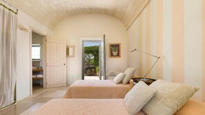 A bedroom with two beds, a wardrobe, a chair, and a desk with a lamp. - 339 I Trulli di Nanì by Perle di Puglia (Ostuni)