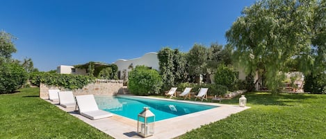 A swimming pool with lounge chairs and a lantern, surrounded by well-maintained grass and trees.