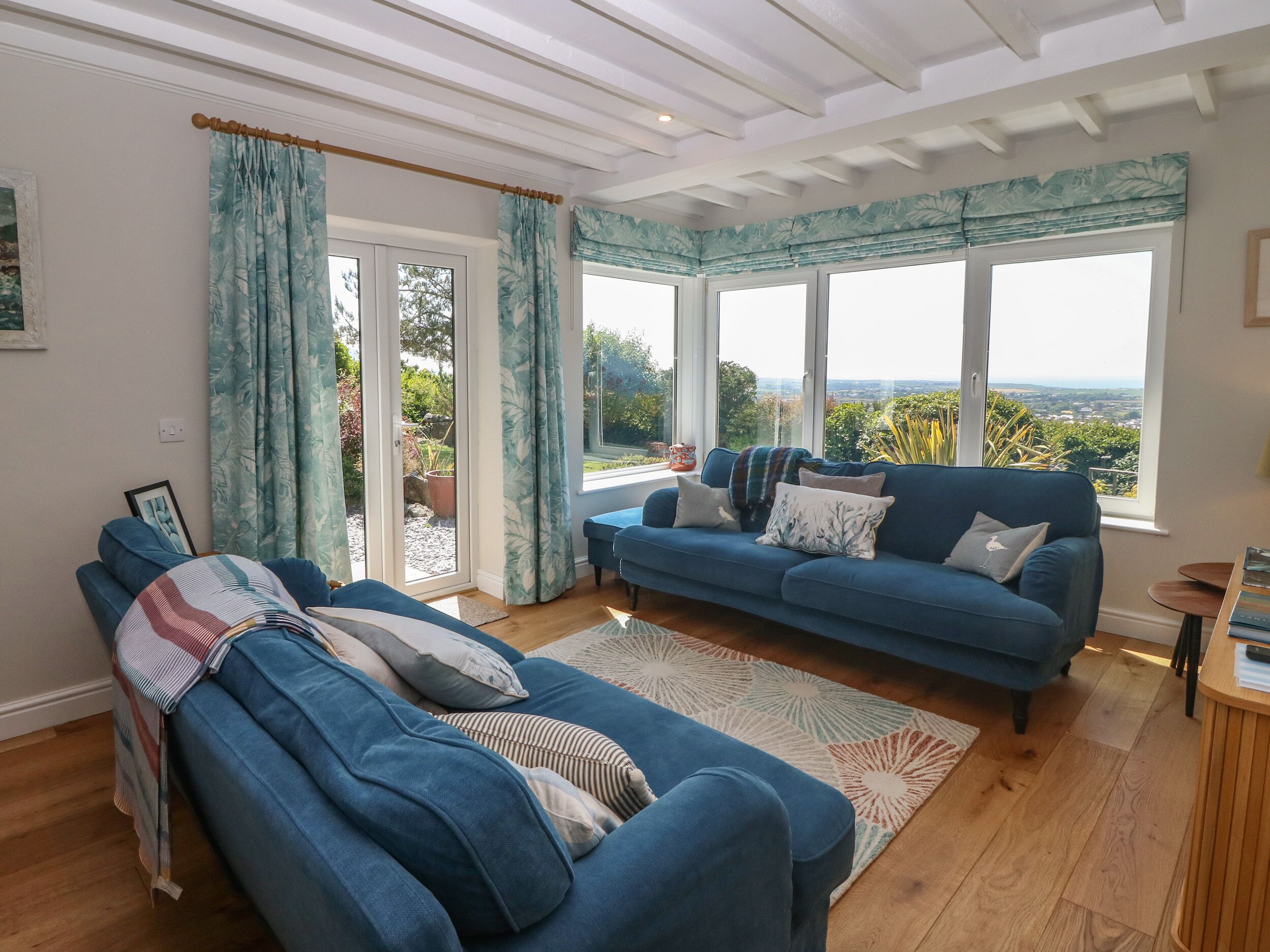 Een woonkamer met een blauwe bank, een blauwe fauteuil en uitzicht op het landschap door grote ramen.