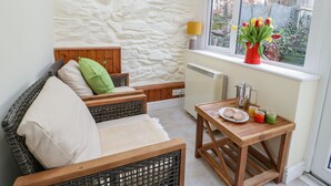 A cozy room with a stone wall, a wooden bed, a wicker chair, a small table with a plate and cups, and a window with a view of the garden. - Dolwen (Betws-Y-Coed)