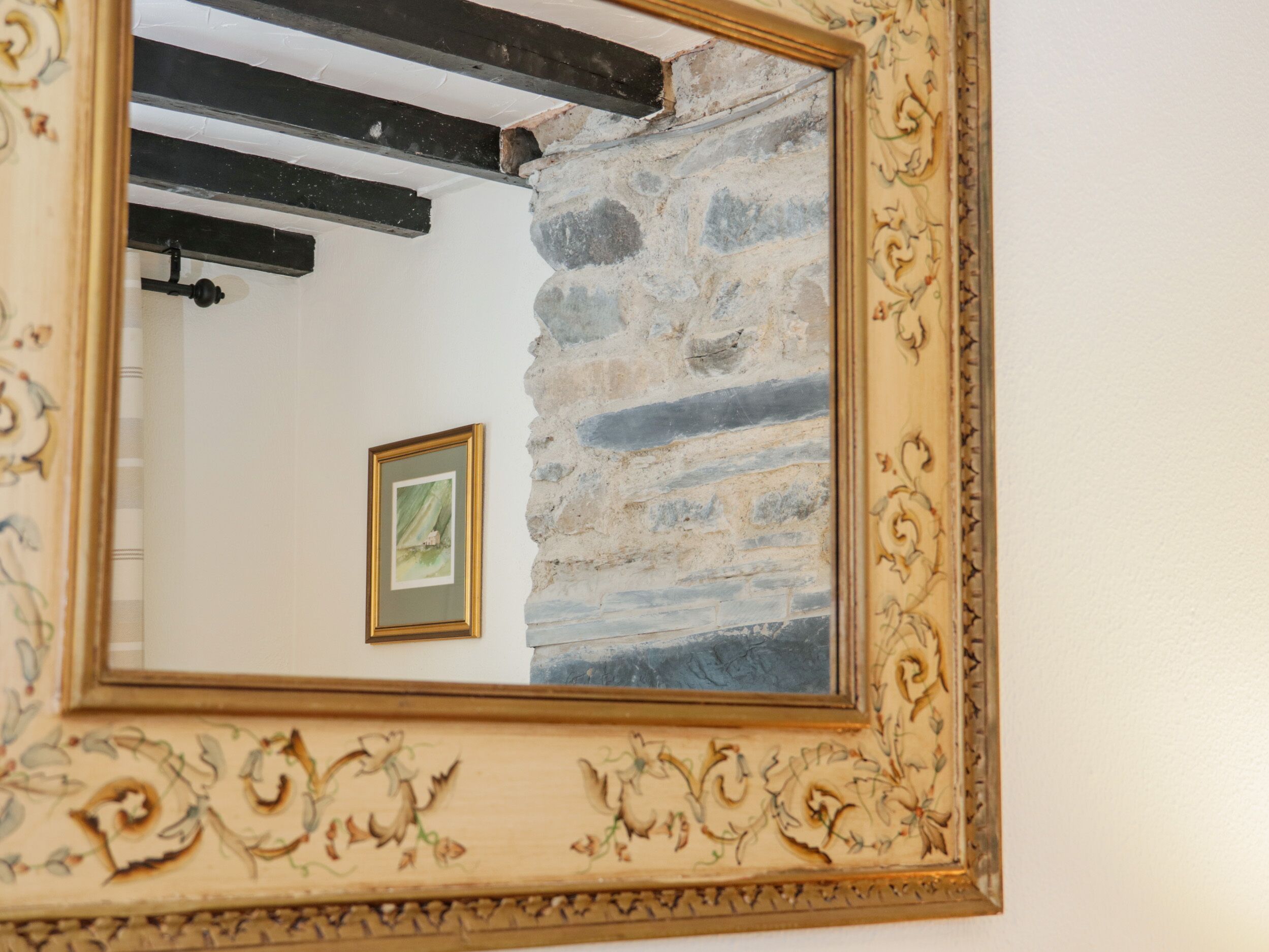 A mirror with a decorative frame reflecting a stone wall and a framed picture.