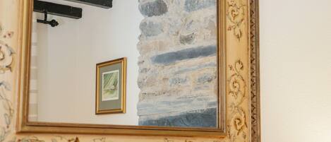 A mirror with a decorative frame reflecting a stone wall and a framed picture.