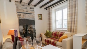 A cozy living room with a stone fireplace, a sofa, a window with curtains, and a tray with wine glasses. - Dolwen (Betws-Y-Coed)