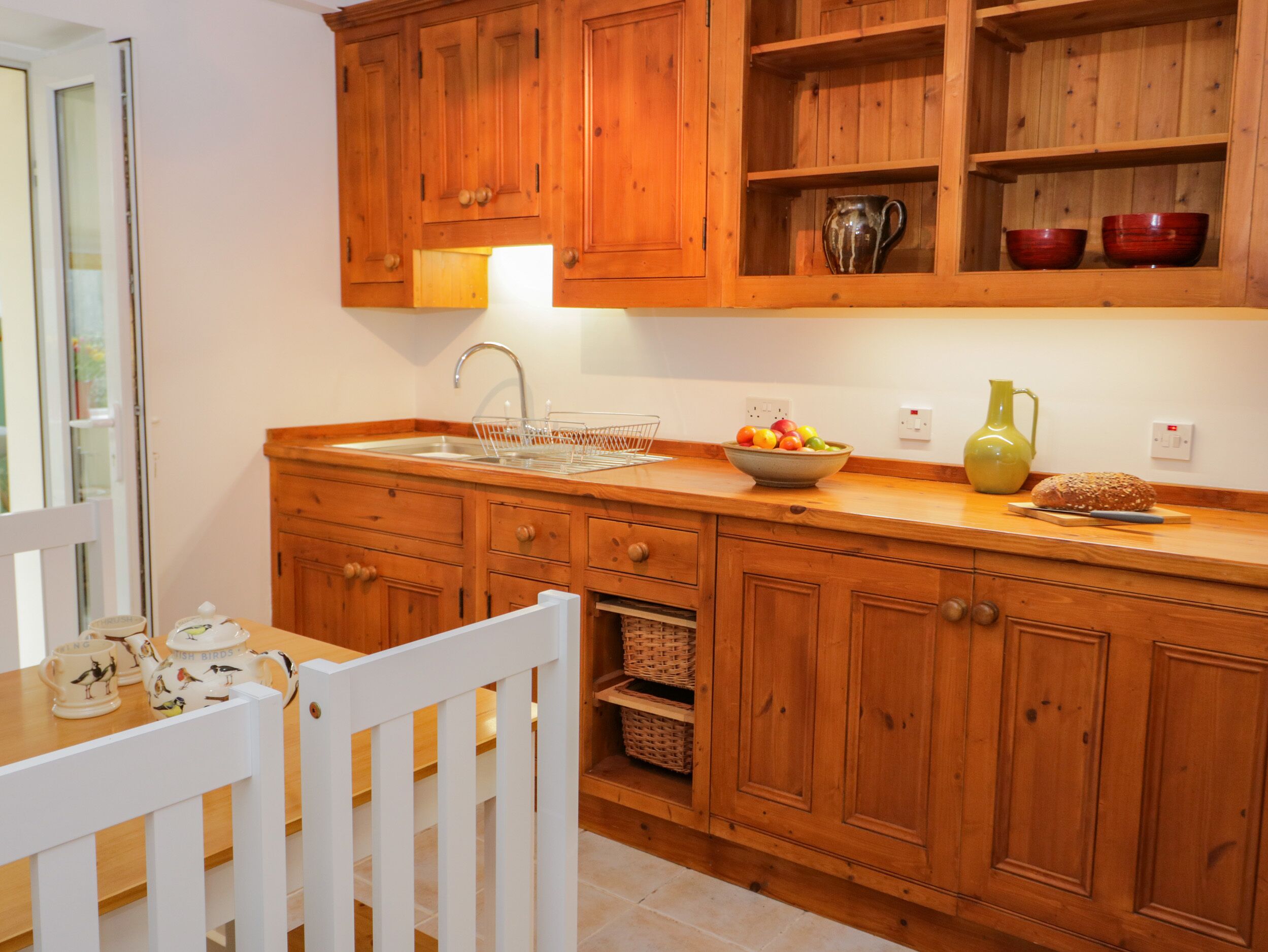 A kitchen with wooden cabinets, a sink, a fruit bowl, and a bread loaf on the counter.