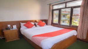 A neatly made bed with a white and red bedspread, a wooden headboard, and a small wooden nightstand with a lamp. - MeroStay 015 (Pokhara)