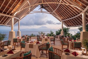 An outdoor dining area with tables and chairs, overlooking a body of water and a mountain.